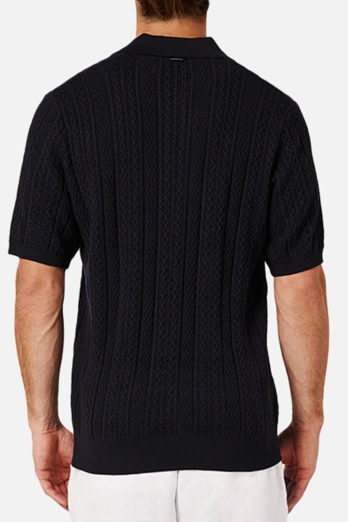 A rear view shows a person in an Industrie The Vito Polo, a black short-sleeve knit sweater with a cable knit finish, paired with white pants against a plain white background.