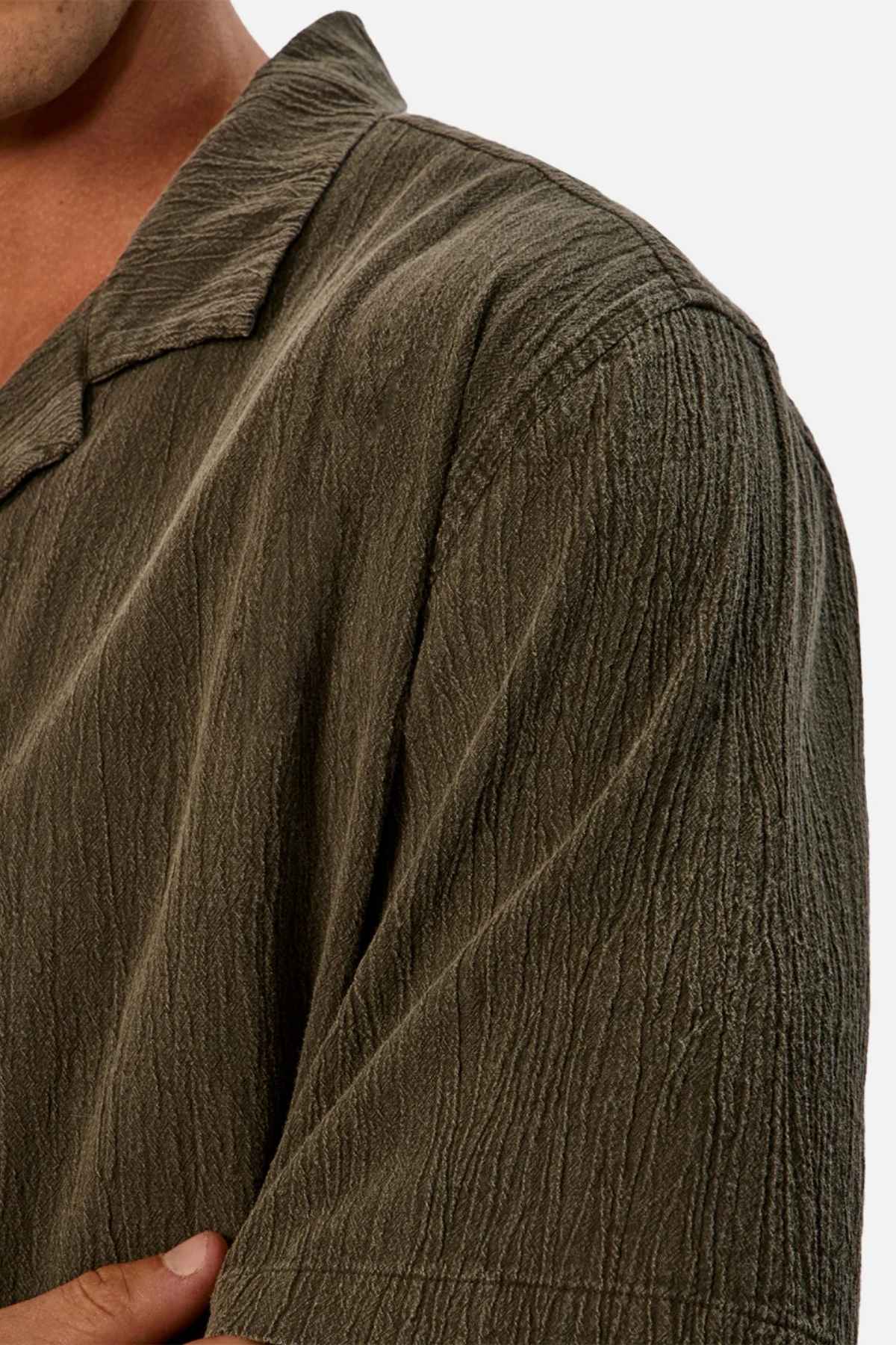 Close-up of a person wearing the Industrie The Washed Magna Short Sleeve Shirt in olive-green. The image focuses on the left shoulder and part of the chest, showcasing the distinctive crinkled pattern and breathable fabric. The oversized fit contributes to a laid-back style against a plain white background.