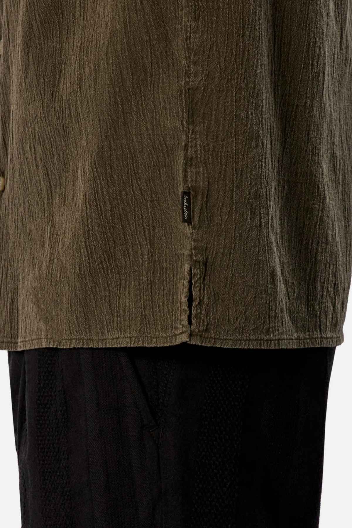 Close-up of a person wearing the Industrie The Washed Magna Short Sleeve Shirt in textured olive green, featuring an oversized fit and a small side label, paired with black pants. The attention is on the breathable fabric and the detail of the shirt's hem.