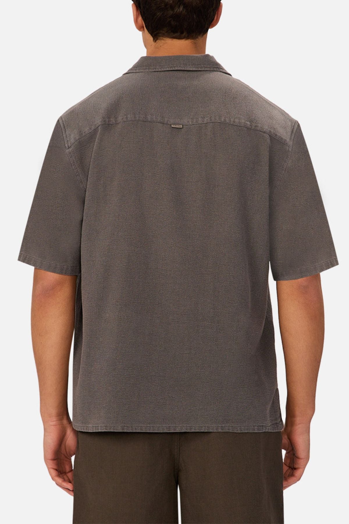A man is shown from behind wearing the Industrie The Washed Menorca Short Sleeve Shirt in gray and dark brown shorts against a plain white background.