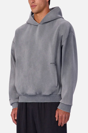 A person wears the Industrie The Washed Tech Hood—a loose-fitting, light gray sweatshirt with long sleeves—paired with dark pants against a plain background, perfect for casual layering.