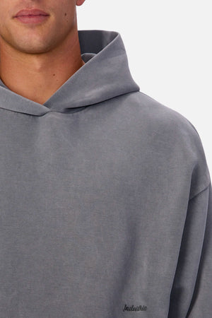 A person wearing the Industrie The Washed Tech Hood—a loose-fitting, faded grey hoodie with a small embroidered "Industrie" chest logo—shown from the shoulders up against a plain background; ideal for casual layering.