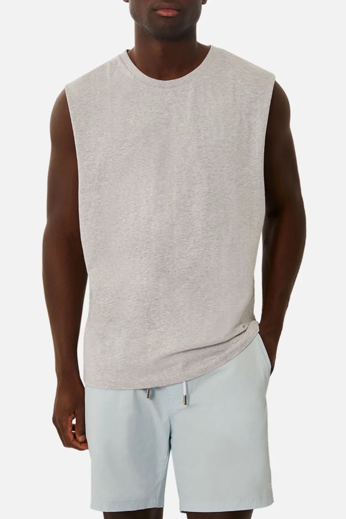 A person wears an Industrie The Triple G Sleeveless Tee in light gray with matching shorts against a plain white background. The relaxed fit complements their stance, left hand casually tucked into their pocket.