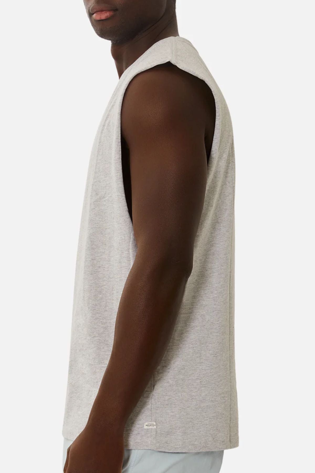 Wearing the Industrie The Triple G Sleeveless Tee made of 100% cotton, a person stands against a white backdrop, slightly turned from the camera. The focus is on their upper body, showcasing the relaxed fit and texture of the gray shirt.