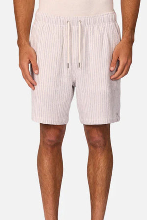 A person wears Industrie The Frescati Short—light-colored, knee-length linen shorts with vertical stripes and a drawstring waistband—standing against a plain, light background with hands relaxed at their sides.