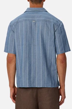 A person is shown from the back against a plain background, wearing an Industrie The Kimridge Short Sleeve Shirt with blue patterns and brown pants.