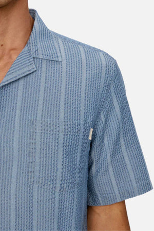 A person wearing the Industrie The Kimridge Short Sleeve Shirt in textured light blue, featuring a collar, shown from shoulders to mid-chest against a plain background.