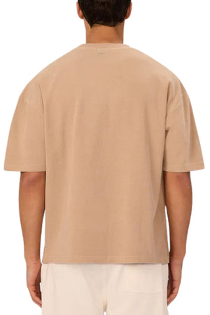 A person stands with their back to the camera wearing the Industrie The Marlon Tee in beige and white pants, ideal for casual wear. The background is plain white.