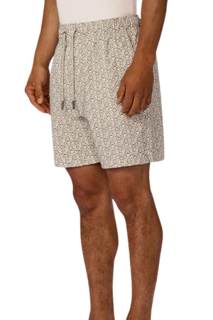 A person models Industrie The Montego Swim Short in a light color with an elastic waistband, drawstring, and subtle Arabesque pattern, standing against a white background with only the lower torso and legs visible.