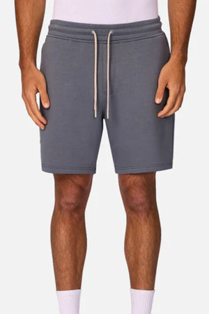 A person wears Industrie The Tech Track Short in gray, styled with a white top and socks, standing against a plain white background. The image is cropped from shoulders to knees.
