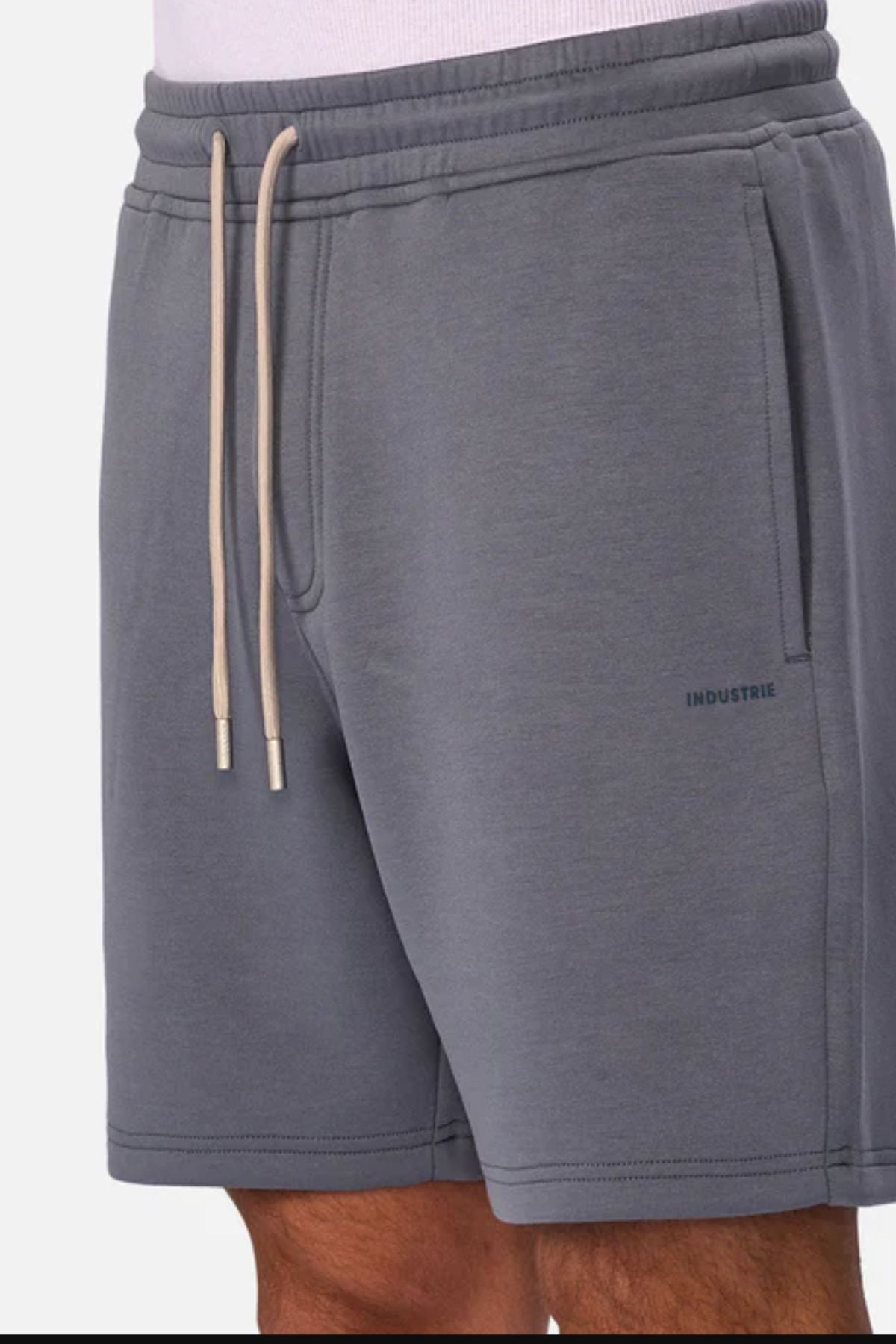 A person wearing Industrie The Tech Track Short in grey, featuring side pockets and "INDUSTRIE" printed near the left hem. Only the lower torso and upper legs are visible.