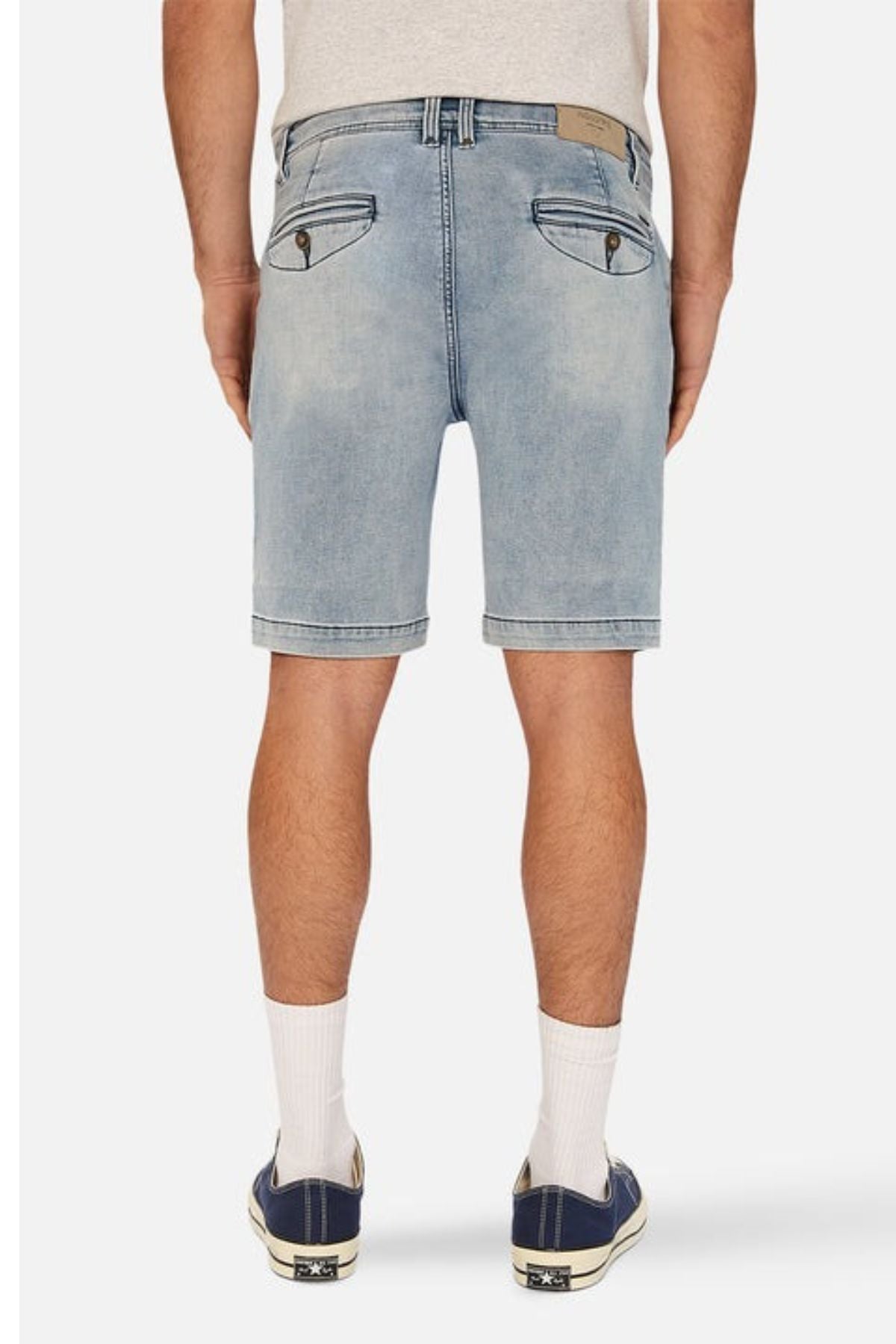 A person wearing a light gray t-shirt, the Industrie The Drifter Denim NC Short in faded blue with a cuffed hem, white knee-length socks, and black sneakers with white soles stands with their back facing the camera.