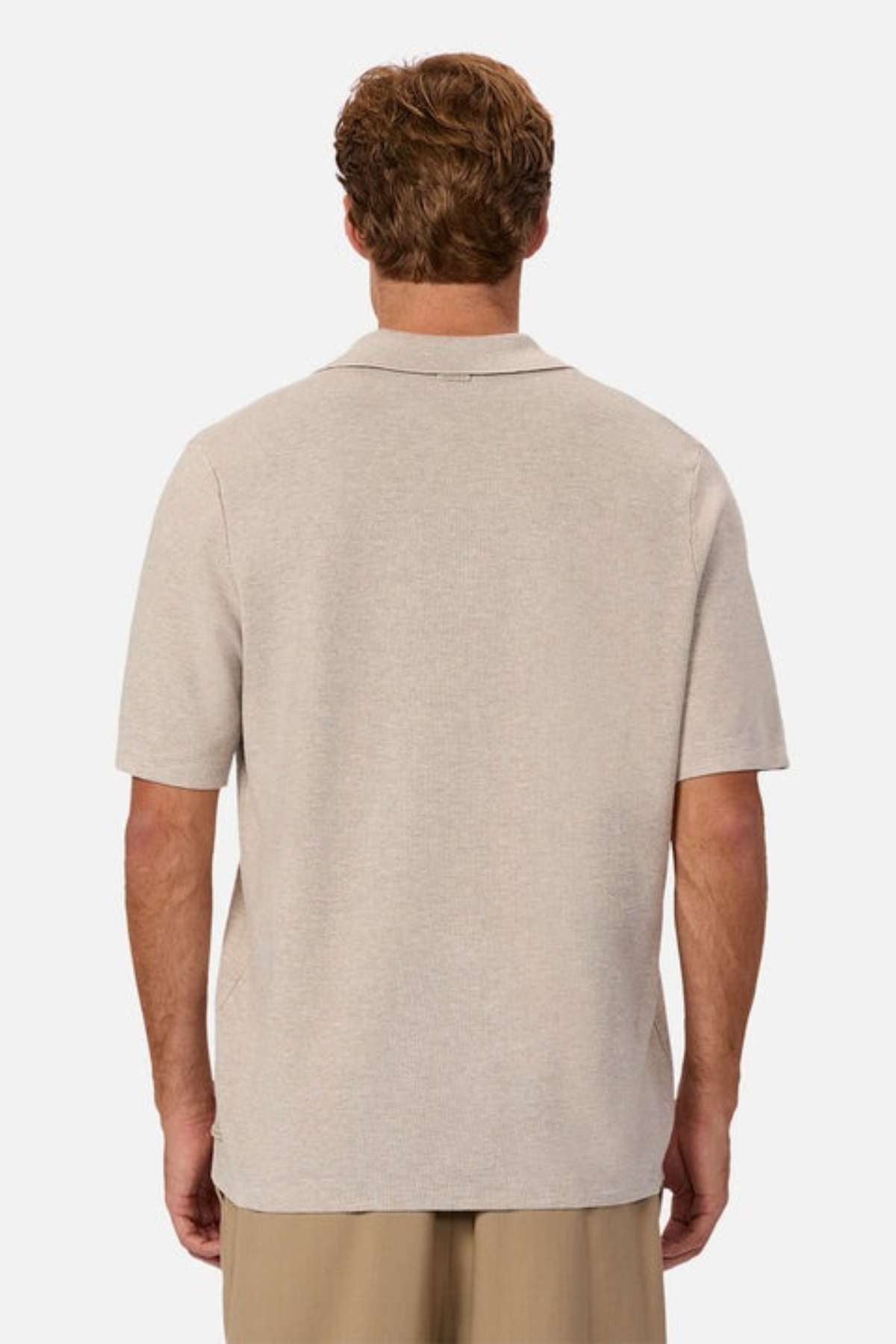 A person with short hair is seen from behind, wearing a light beige Industrie The Hampshire Polo. Embracing a casual style with light brown pants, the individual exemplifies comfort. The Hampshire Polo featured adds a touch of sophistication, standing out against the plain white background.