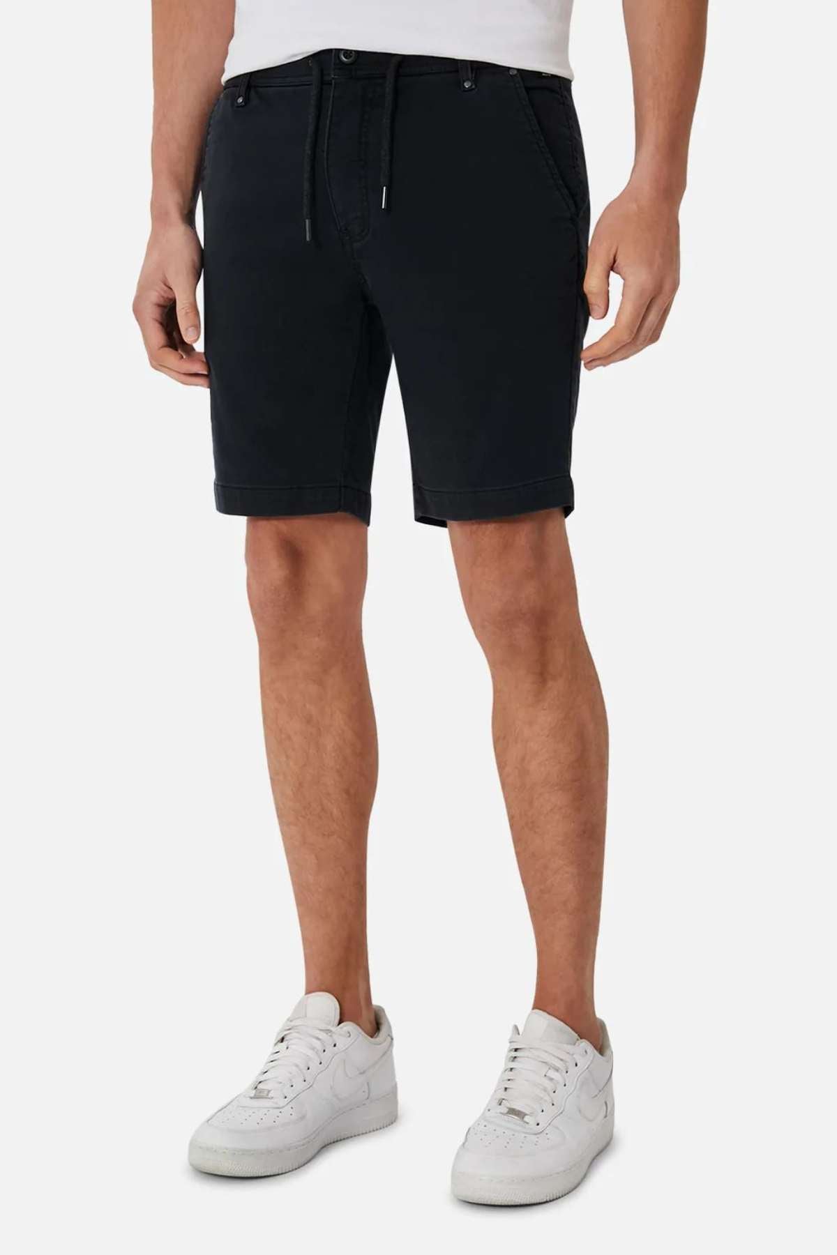A person is sporting the Industrie The New Drifter Cuba Short, known for its modern slim fit and comfortable belt-loop waist, teamed with white sneakers. The shorts are equipped with side pockets and boast a fitted design. Additionally, the individual is wearing a white shirt, though only the lower section is visible against a plain white background.
