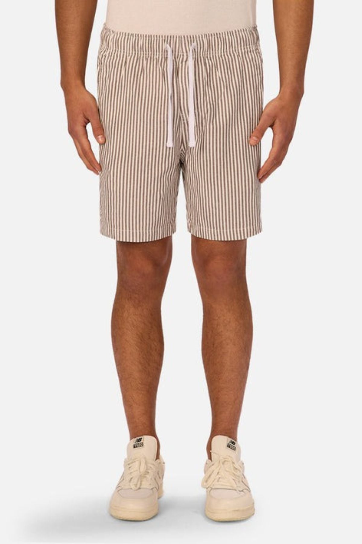 A person wears beige and white vertical striped Industrie The New Southwest Short linen shorts and white sneakers, standing against a plain light background. The image is cropped from the waist down to highlight the classic style of the shorts.