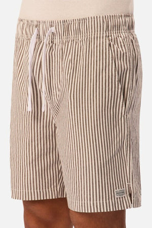 A person wears beige and white vertical striped linen men’s shorts with an elastic waistband, white drawstring, side pockets, and a small rectangular label near the hem: Industrie The New Southwest Short.