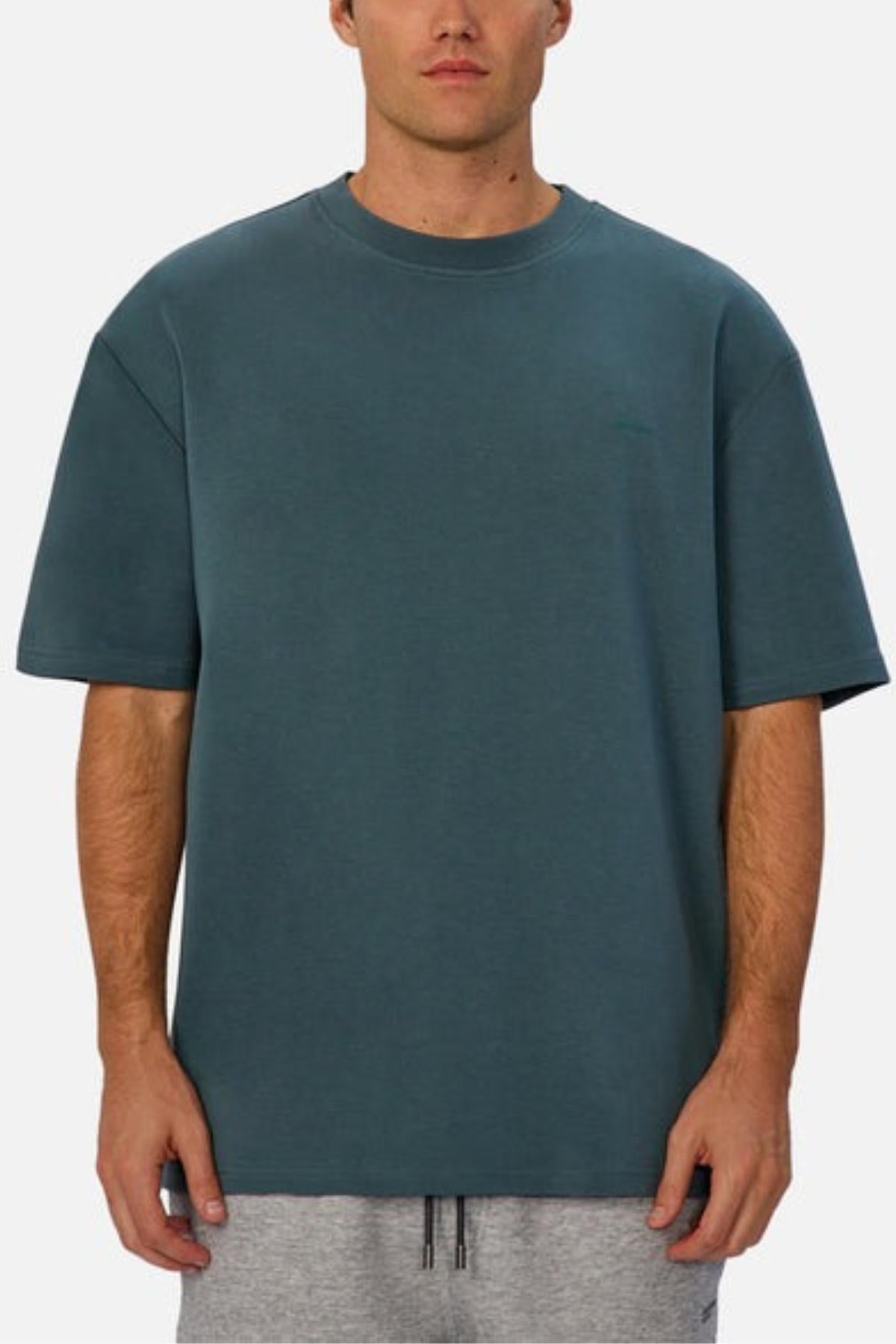 Someone wears the Industrie The Newport Tee, a loose-fitting, oversized heavyweight teal shirt, paired with light gray drawstring shorts and shown from the front on a plain white background—ideal for relaxed, casual style.