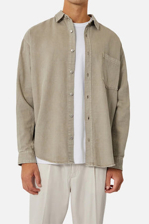 A person dons the Industrie The Portland Shirt, a beige cotton-linen overshirt, paired with a white t-shirt and matching beige pants. The ensemble offers a relaxed fit with long sleeves, a collar, and chest pocket, set against a plain white background.
