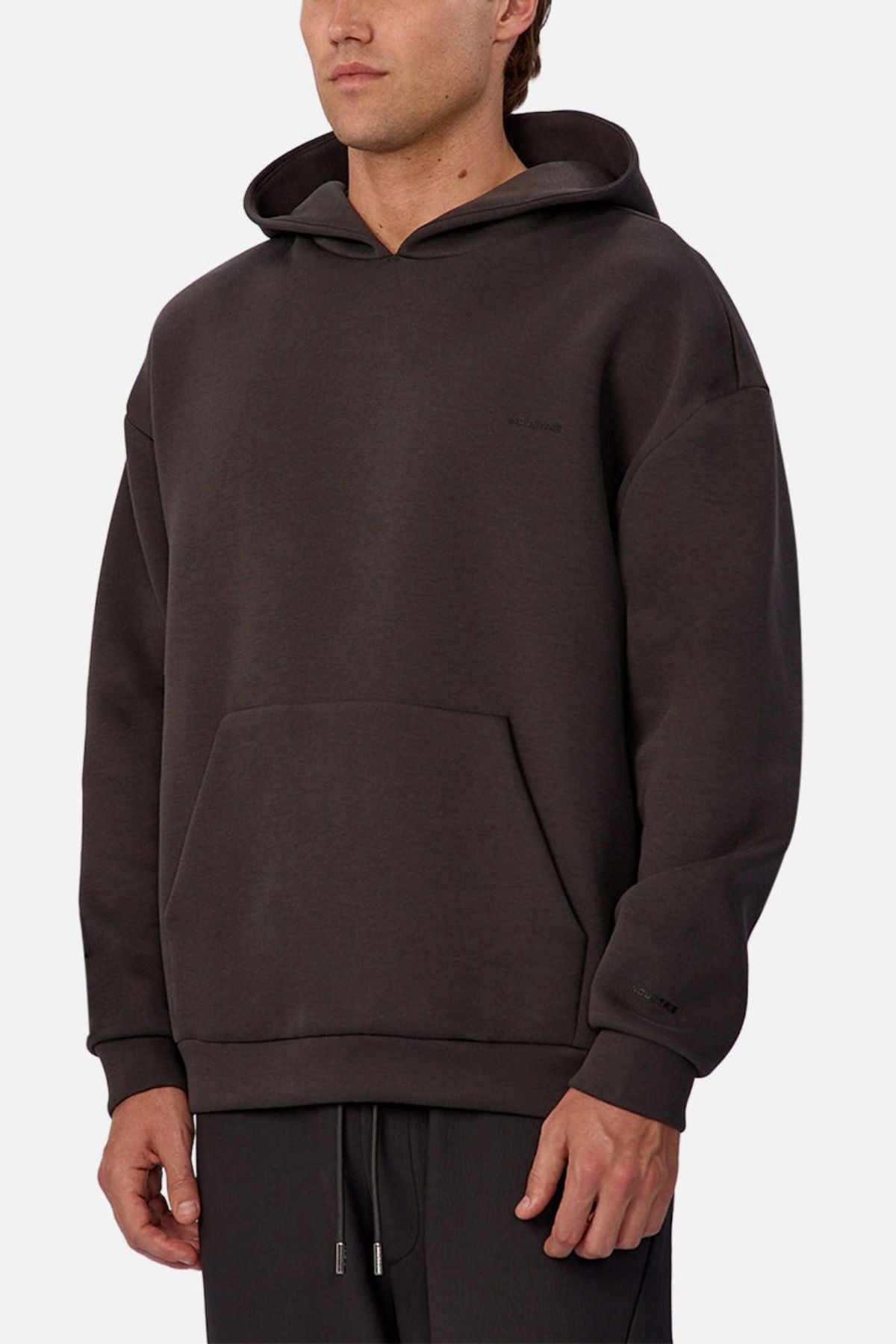 A man wearing the Industrie The Tech Del Sur Hoodie in dark brown, featuring a loose fit, front kangaroo pocket, and matching drawstring pants, stands against a plain white background.