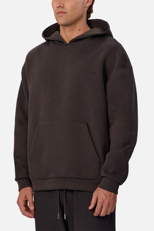 A man wearing the Industrie The Tech Del Sur Hoodie in dark brown, featuring a loose fit, front kangaroo pocket, and matching drawstring pants, stands against a plain white background.