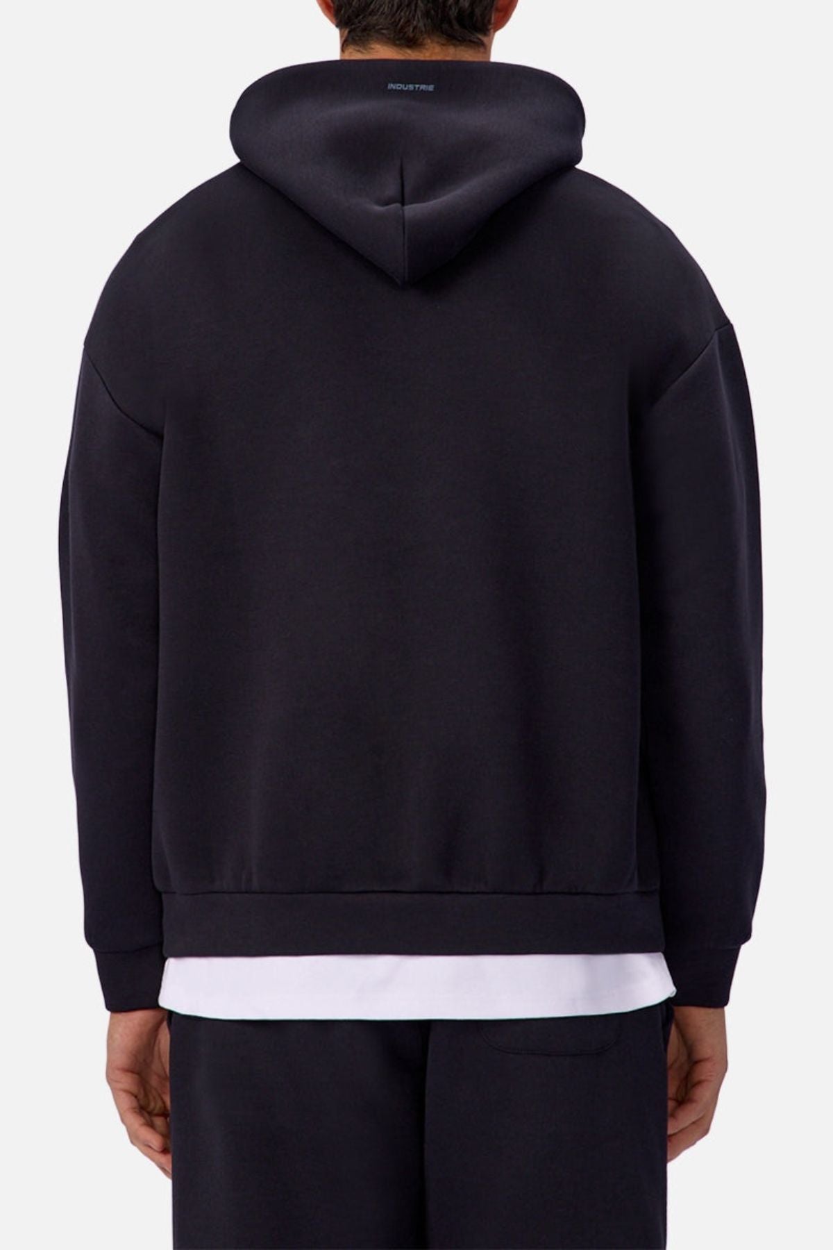 A person is seen from the back wearing the Industrie The Tech Del Sur Hoodie in black over a white shirt and black pants, standing against a plain light background.