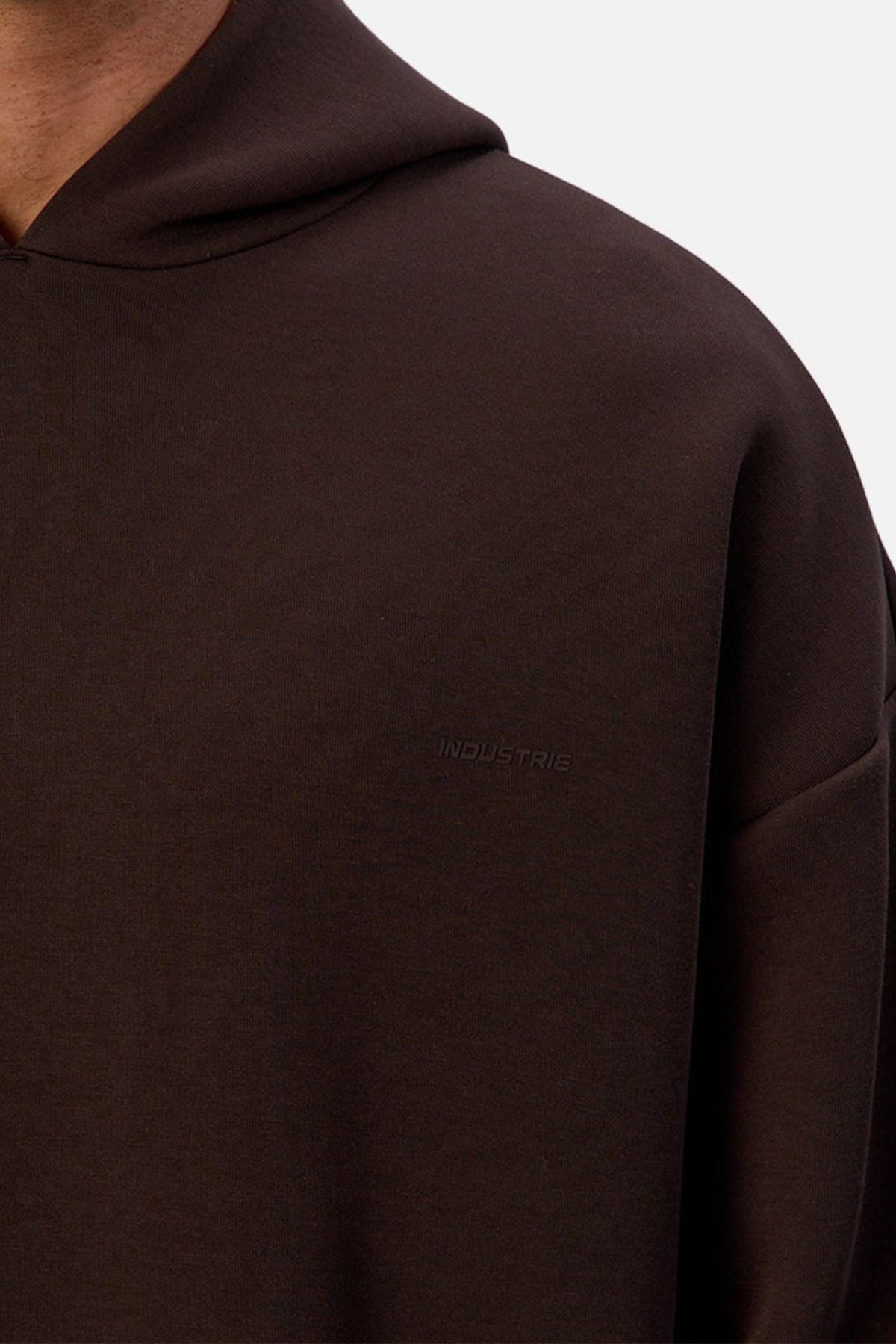 Close-up of a person wearing the Industrie The Tech Del Sur Hoodie, featuring breathable athletic fabric and discreet “INDUSTRIES” embroidery on the chest. The focus is on the upper torso and shoulder against a plain background.