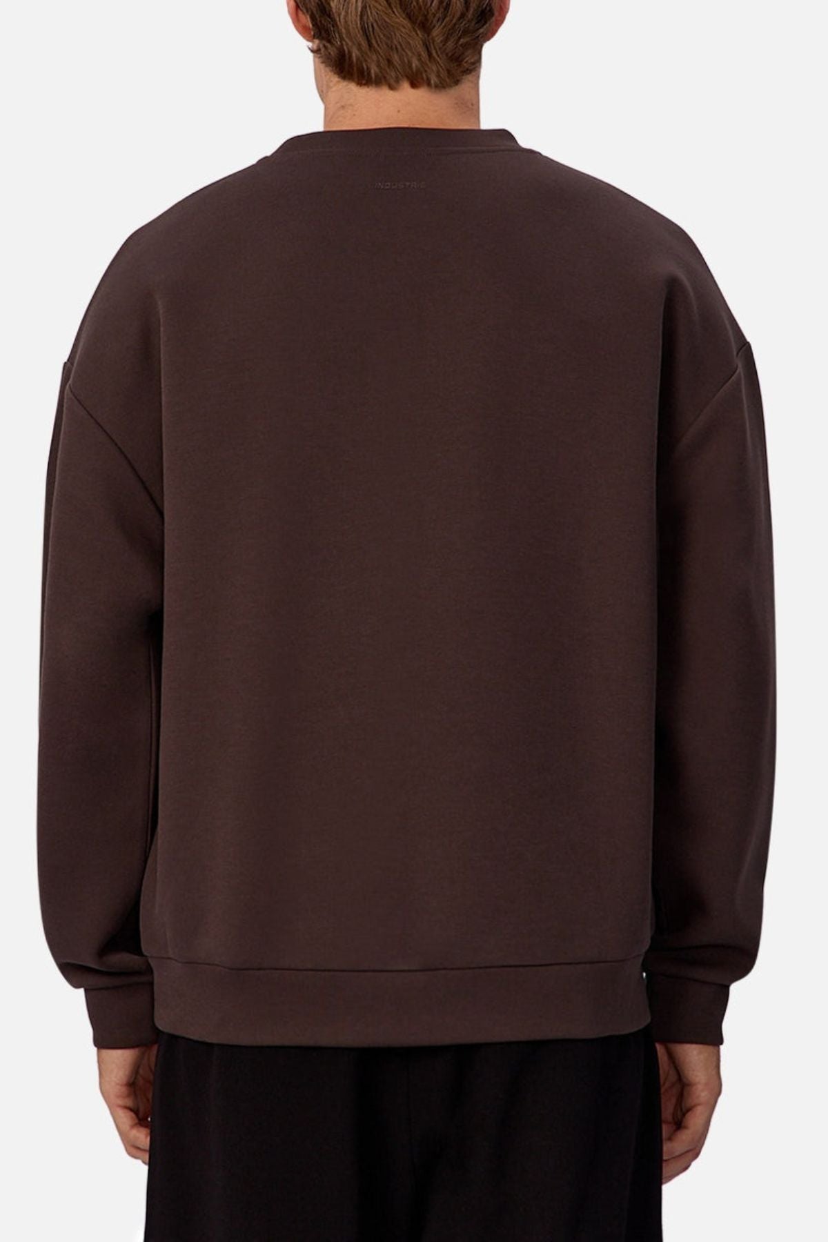 A person with short light brown hair is shown from the back, wearing an oversized Industrie The Tech Del Sur Sweat and black pants against a plain light background.