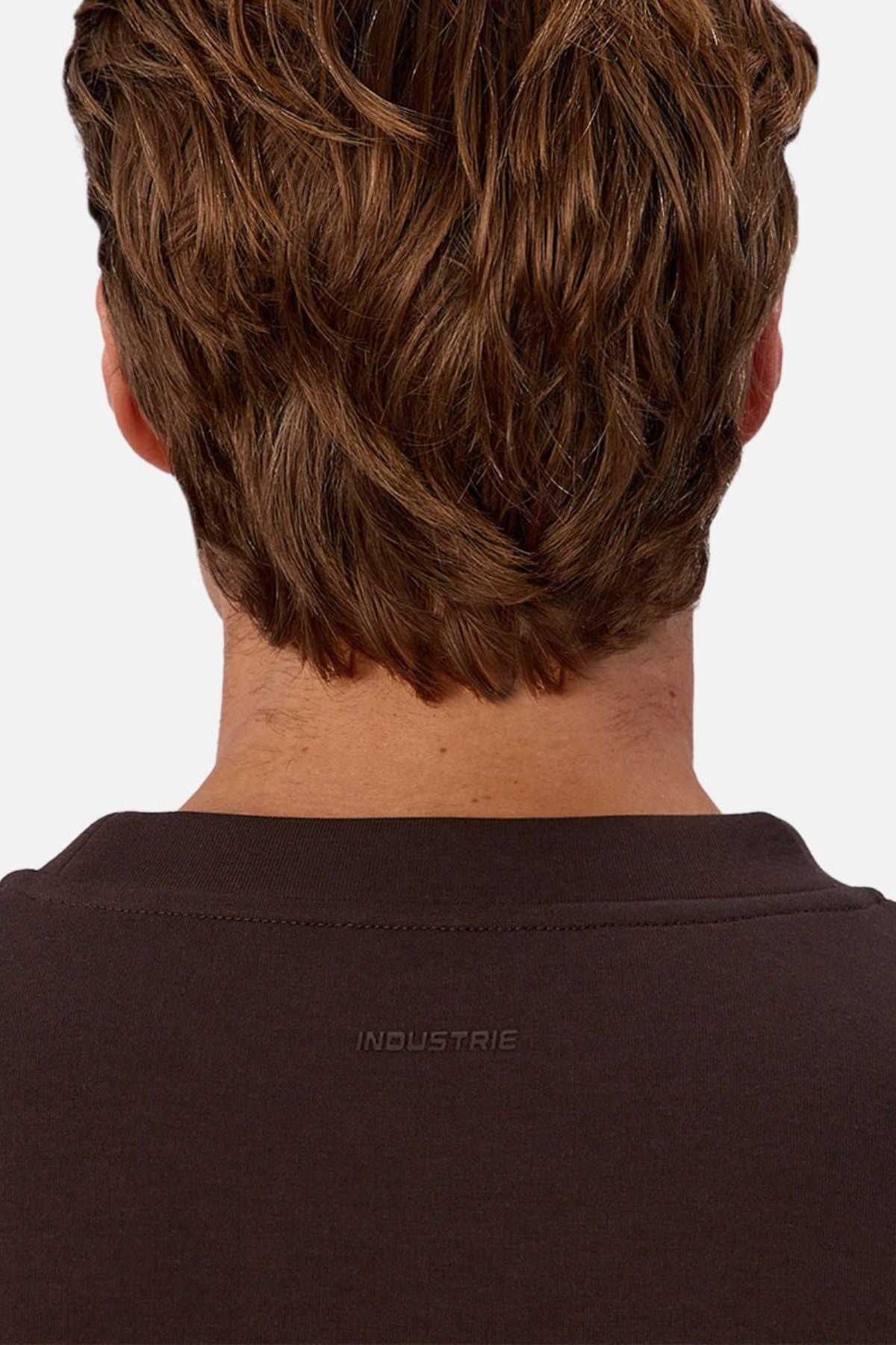The image shows the back of a person with short, wavy brown hair wearing a dark brown Industrie The Tech Del Sur Sweat, featuring "INDUSTRIE" subtly printed on the upper back.