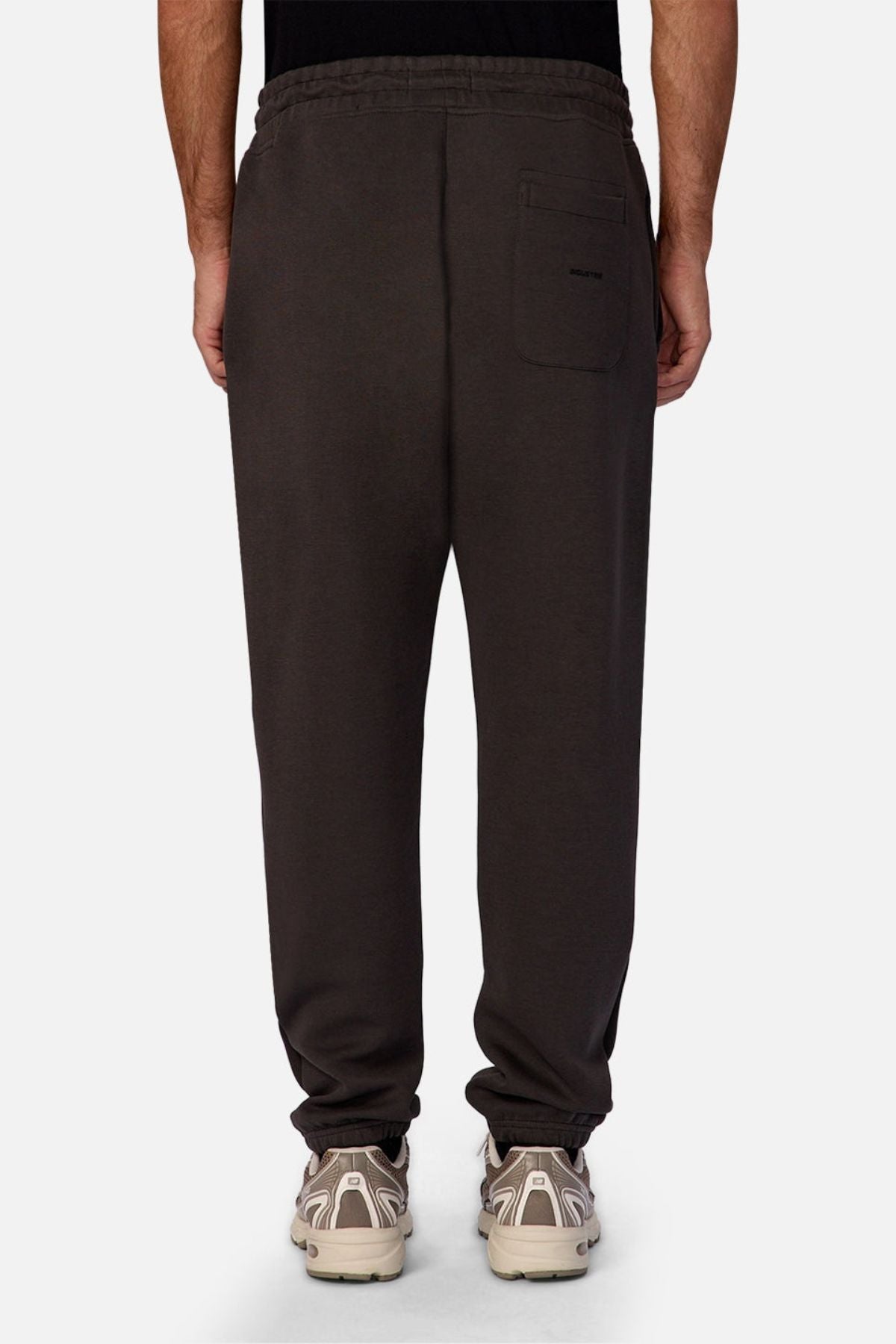 A person is seen from the back wearing Industrie The Tech Del Sur Track Pant in dark gray athletic material, styled with white sneakers. The pants feature an elastic waistband, single back pocket, and are set against a light background.