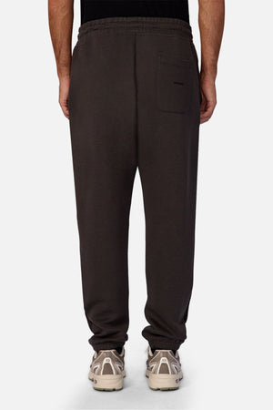 A person is seen from the back wearing Industrie The Tech Del Sur Track Pant in dark gray athletic material, styled with white sneakers. The pants feature an elastic waistband, single back pocket, and are set against a light background.