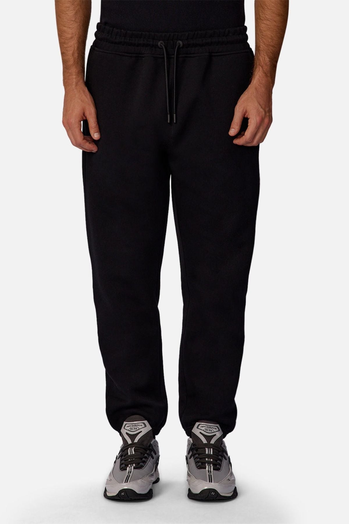 A person models the Industrie The Tech Del Sur Track Pant in black with a drawstring waist, paired with gray athletic shoes against a plain white background. The image is cropped from the chest down.