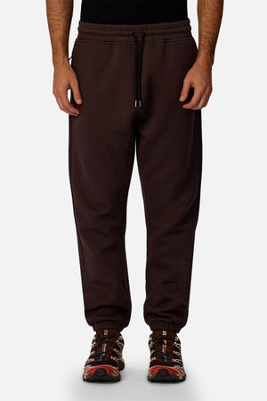 Someone wears the Industrie The Tech Del Sur Track Pant in dark brown, featuring an elastic waistband and drawstring, made from athletic fabric, styled with multicolored sneakers against a plain light background.