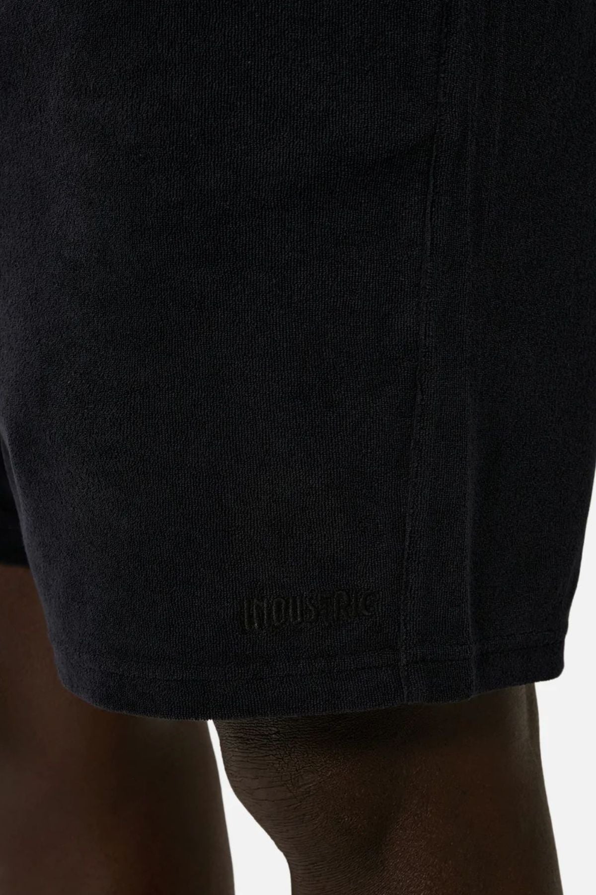 Close-up image of a person's upper legs wearing the Industrie The Wynwood Short, crafted for an ideal summer style. The black men's shorts display understated branding near the hem, set against a neutral background.