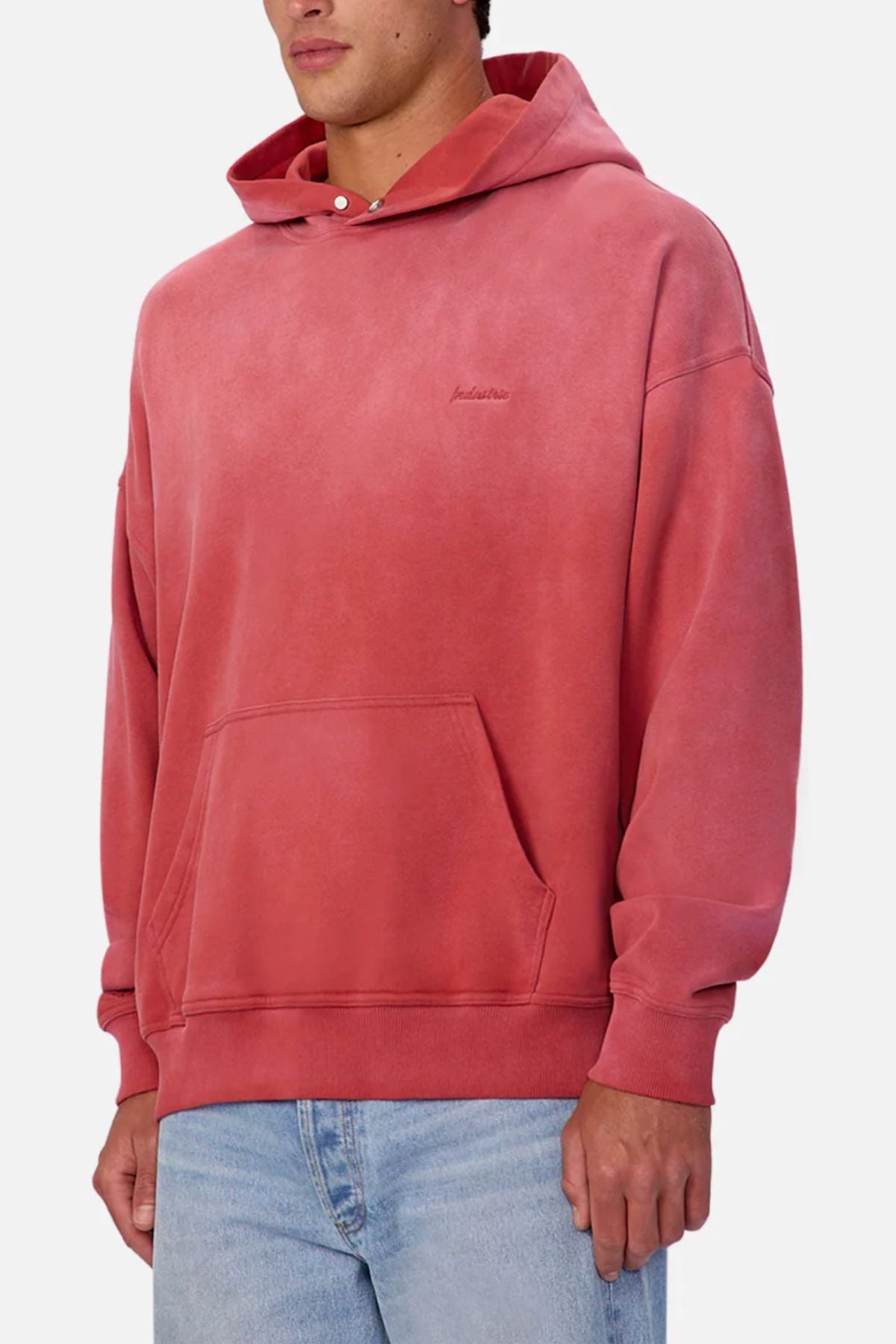 Someone wearing the Industrie The Sandblast Hoodie in faded pink, made from 100% cotton with a front pocket, paired with light blue jeans. Shown from the chest down against a plain background for a relaxed vibe.