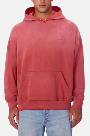 A man wearing the Industrie The Sandblast Hoodie in faded red with a front pocket and subtle left chest text, paired with blue jeans, stands against a plain light background. The 100% cotton hoodie is ideal for a laid-back look.