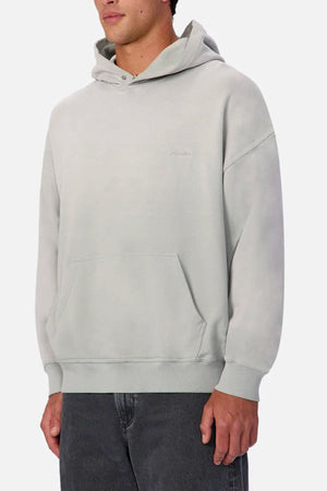 Someone stands against a plain white background wearing the Industrie The Sandblast Hoodie in light gray, crafted from 100% cotton with a front pocket, paired with dark gray jeans for a relaxed, laid-back style.