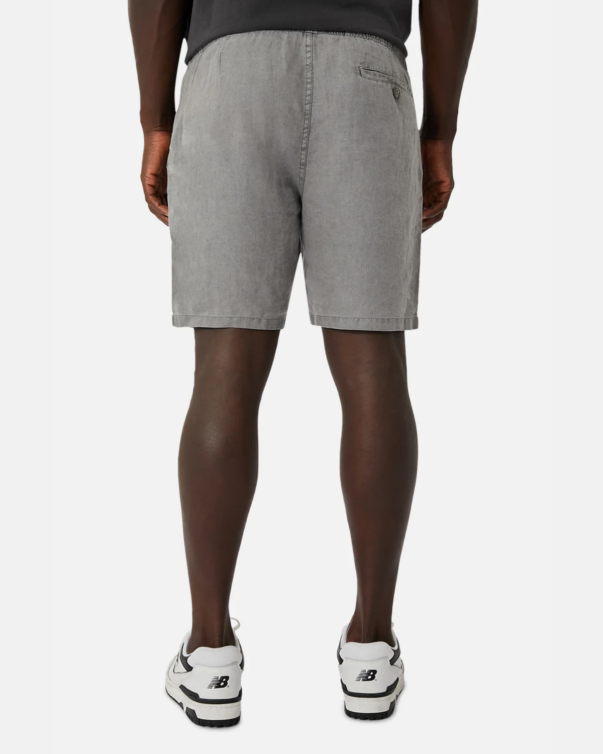A person is seen from behind wearing gray denim shorts with pockets, similar in style to Industrie The Marina Linen Short, and white sneakers with black accents against a crisp white background.