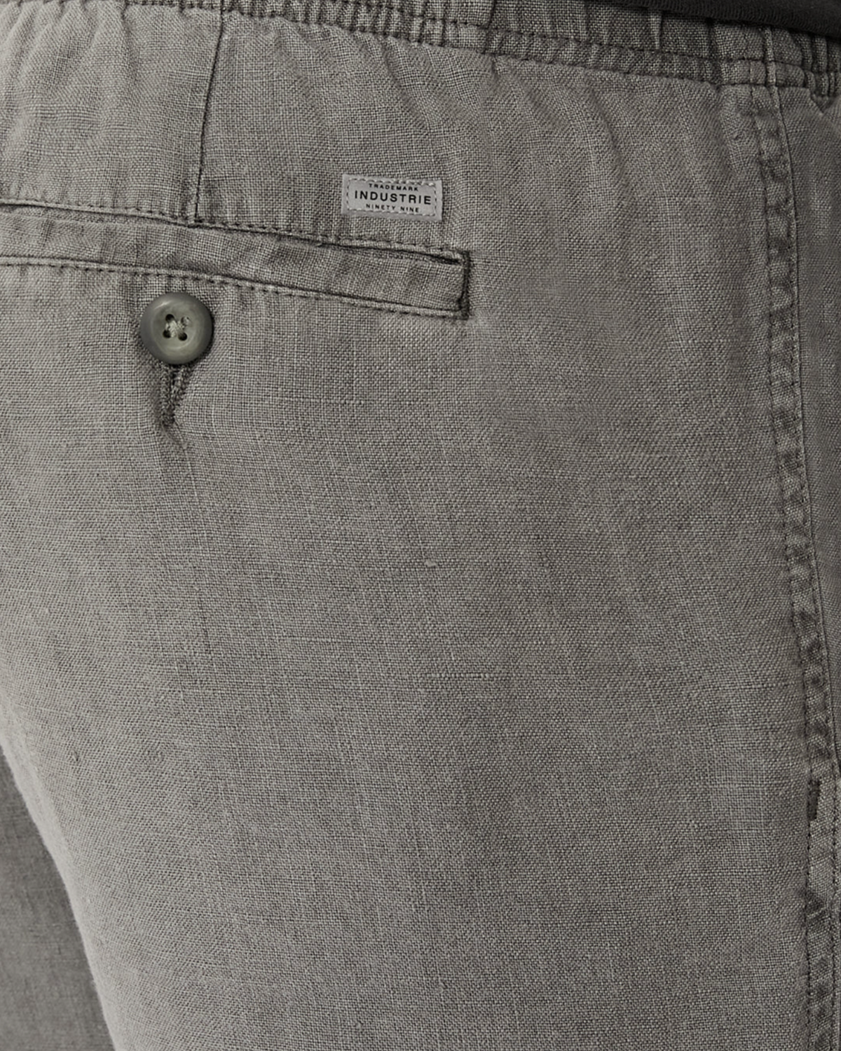 Close-up of the back pocket on Industrie The Marina Linen Short in relaxed-fit gray, featuring a button, small white "INDUSTRIE" label, visible fabric texture, stitching details, and a drawcord waist.