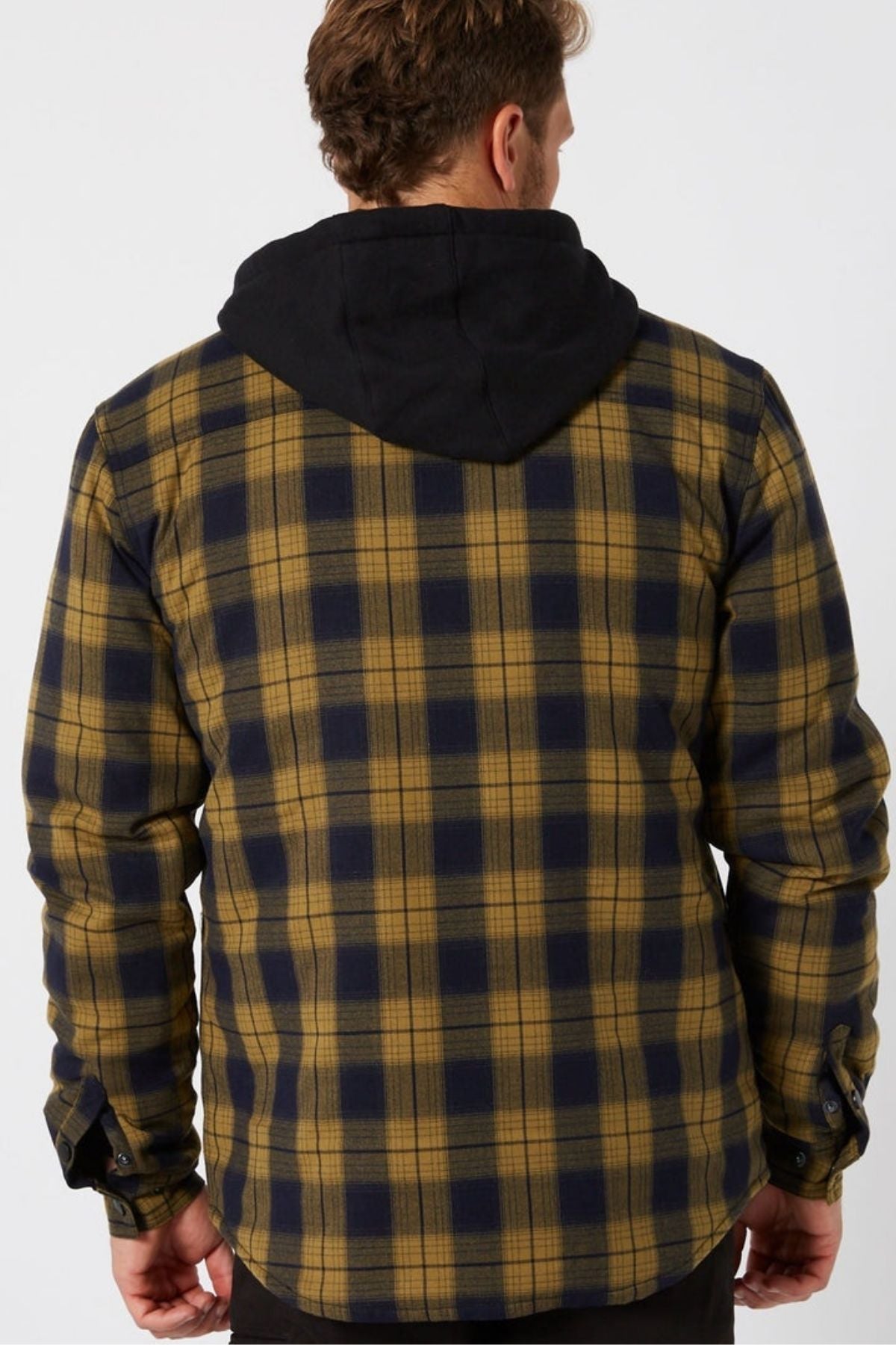 A man faces away from the camera, wearing a Jetpilot Quilted Flannel Jacket in yellow and navy with a black hood. The background is plain and light-colored.