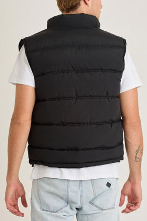 A light-haired person is seen from the back wearing a white T-shirt, light blue jeans, and a Jetpilot Zip Up Vest. There is a small tattoo near their right elbow.