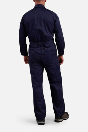 A person stands facing away from the camera, wearing King Gee Combination Drill Overalls and black-and-gray shoes, set against a plain white background.