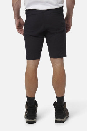 A man, seen from behind against a plain white background, wears black King Gee Workcool Pro Shorts made from Ripstop stretch fabric, paired with a white shirt, black socks, and dark hiking shoes.