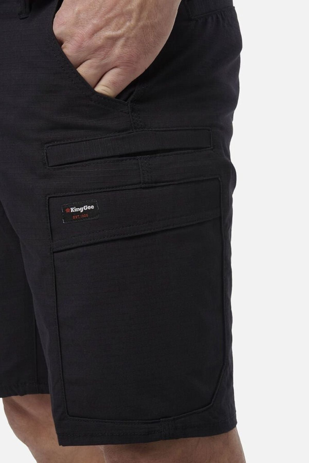 A person wears King Gee Workcool Pro Shorts in black with a hand in the pocket, showcasing multiple pockets, Ripstop stretch fabric, and detailed stitching.