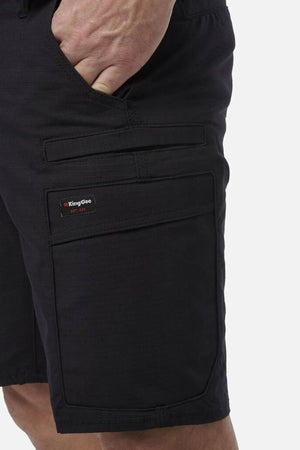 A person wears King Gee Workcool Pro Shorts in black with a hand in the pocket, showcasing multiple pockets, Ripstop stretch fabric, and detailed stitching.