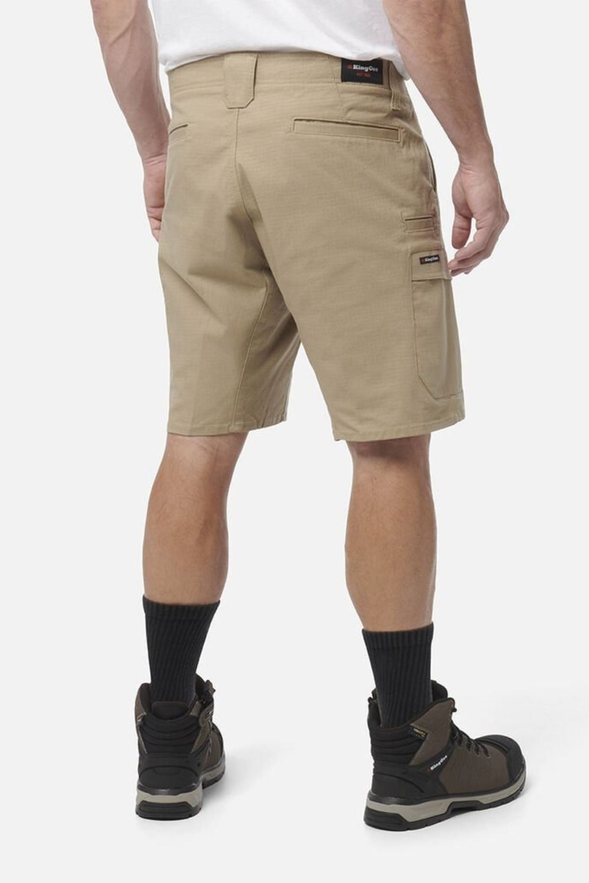 A man wearing King Gee Workcool Pro Shorts, a white shirt, black crew socks, and brown work boots stands with his back to the camera against a plain white background.