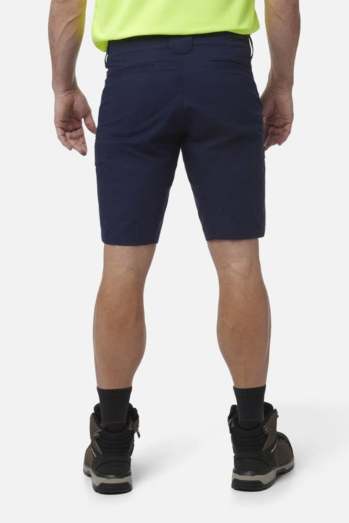 A person is seen from the back wearing King Gee Workcool Pro Shorts, black socks, brown work boots, and a fluorescent yellow shirt against a plain white background.