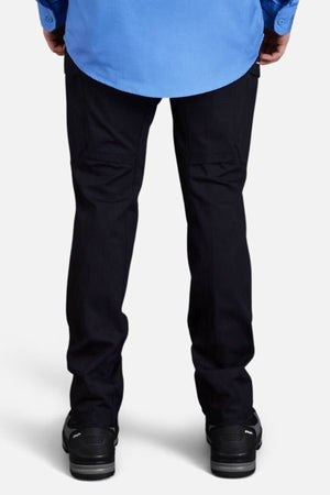 A person, seen from behind, wears a light blue shirt and King Gee Workcool Pro Stretch Cargo Pant with multifunctional pockets and black shoes, standing against a plain light background.