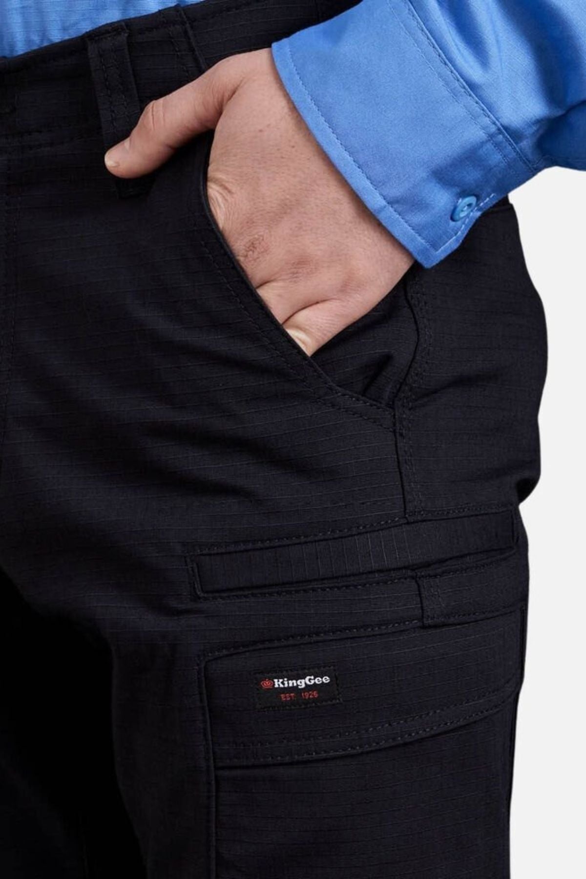 A person in a blue shirt slips their hand into the pocket of King Gee Workcool Pro Stretch Cargo Pants, featuring a visible KingGee logo on the zippered side pocket and multiple multifunctional pockets for extra utility.