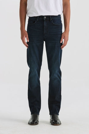 A person wearing a white t-shirt, Lee Originals L100 Slim Jean with a comfortable fit, and black shoes stands against a plain light background. The image is cropped from the shoulders down.