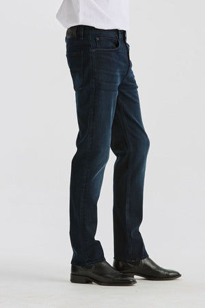 A person wears Lee Originals L100 Slim Jean and black dress shoes, standing against a plain white background. Only the lower half is visible, highlighting the comfortable fit of the jeans.